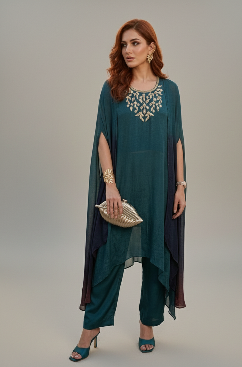 Woman wearing a teal outfit with a cape and jewelry on a gray background