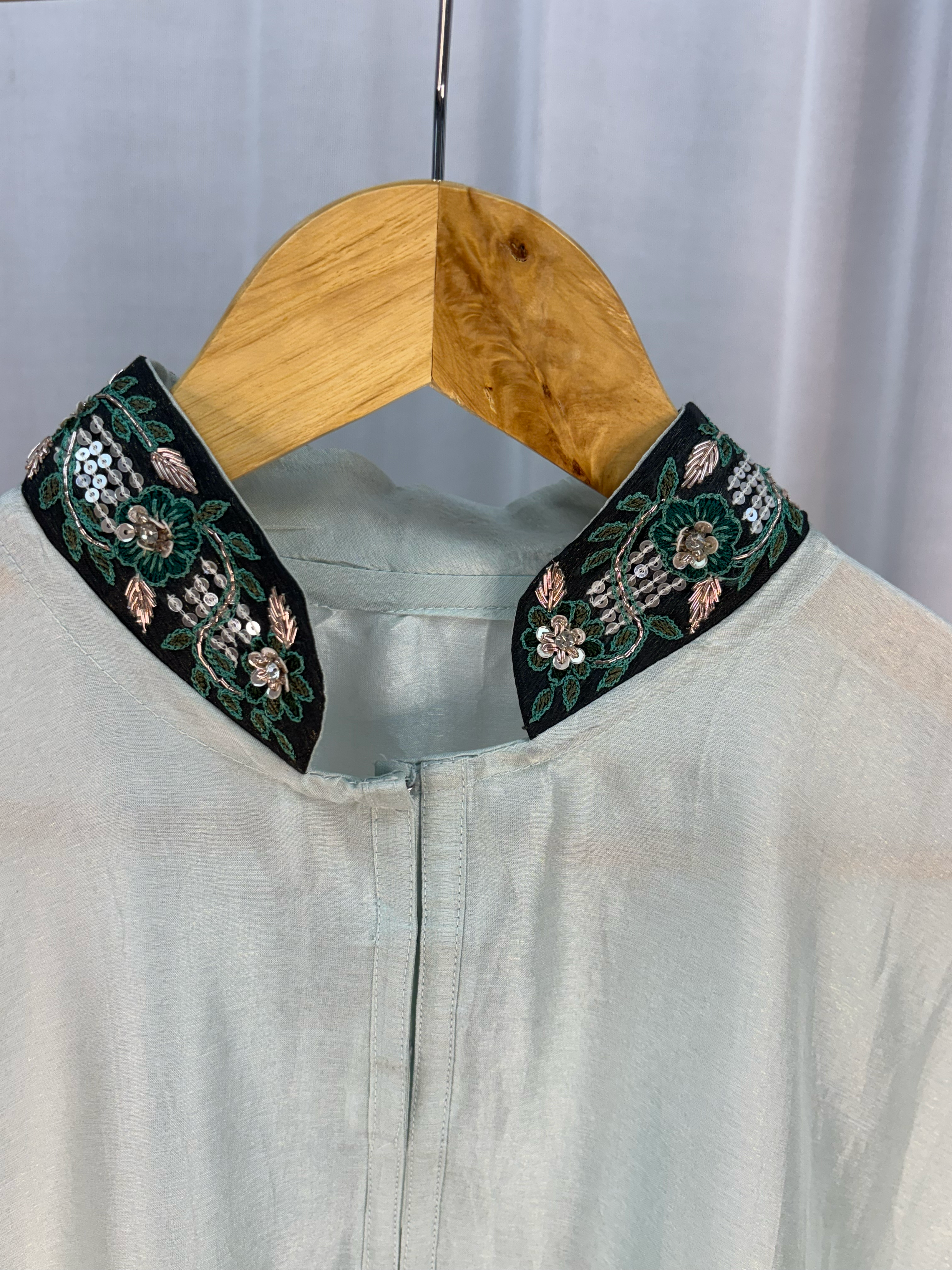 Light-colored garment with embroidered green collar on a hanger against a white background