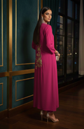 Woman in a pink dress with floral embroidery standing in a dimly lit room.