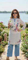 Woman in a striped outfit with floral embroidery standing by a body of water.