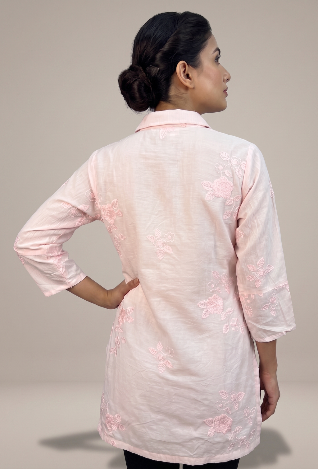 Woman wearing a light pink embroidered kurta against a neutral background