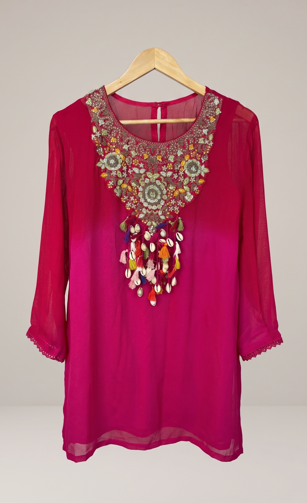 Pink blouse with intricate embroidery on a wooden hanger against a plain background