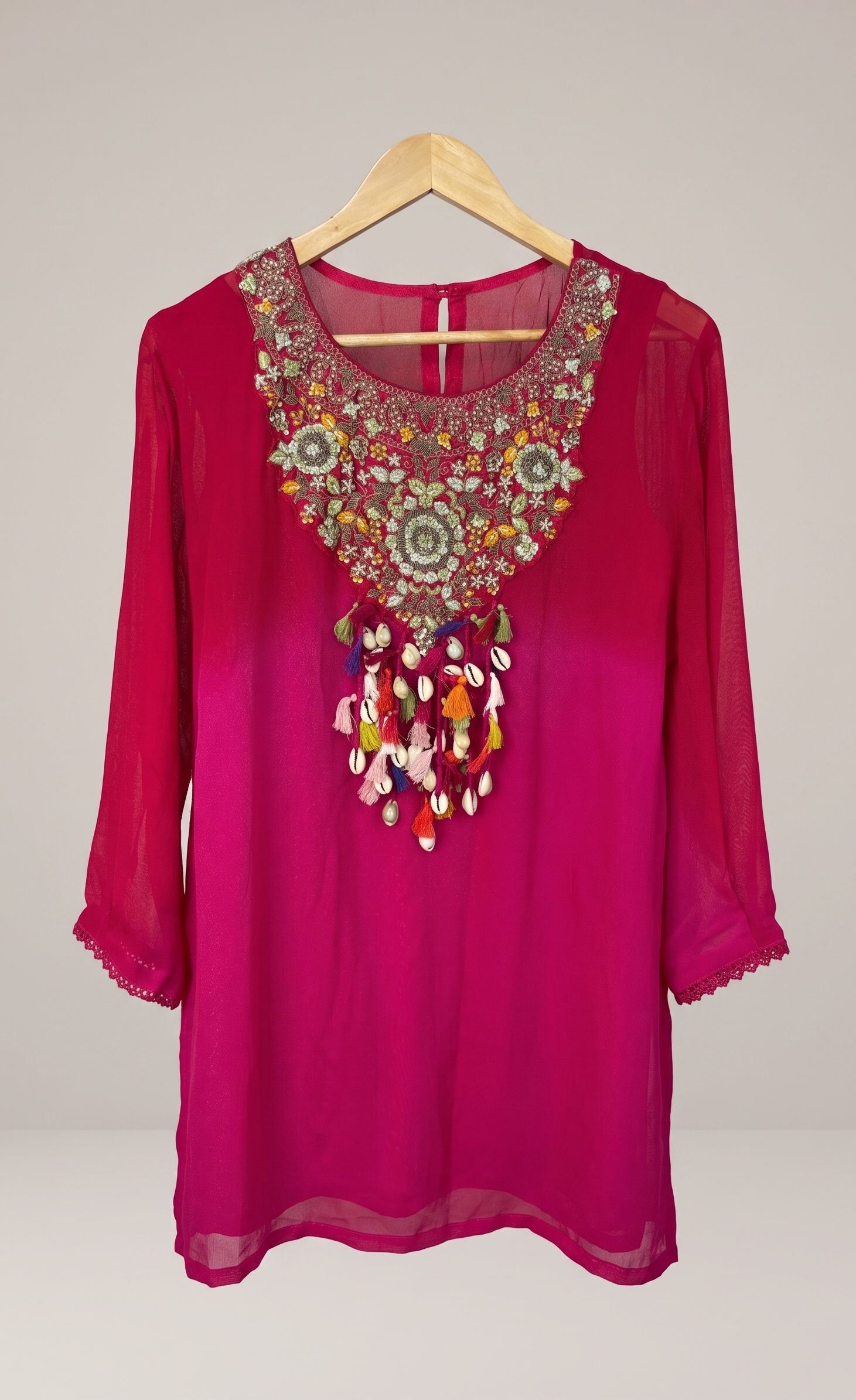 Pink blouse with intricate embroidery on a wooden hanger against a plain background