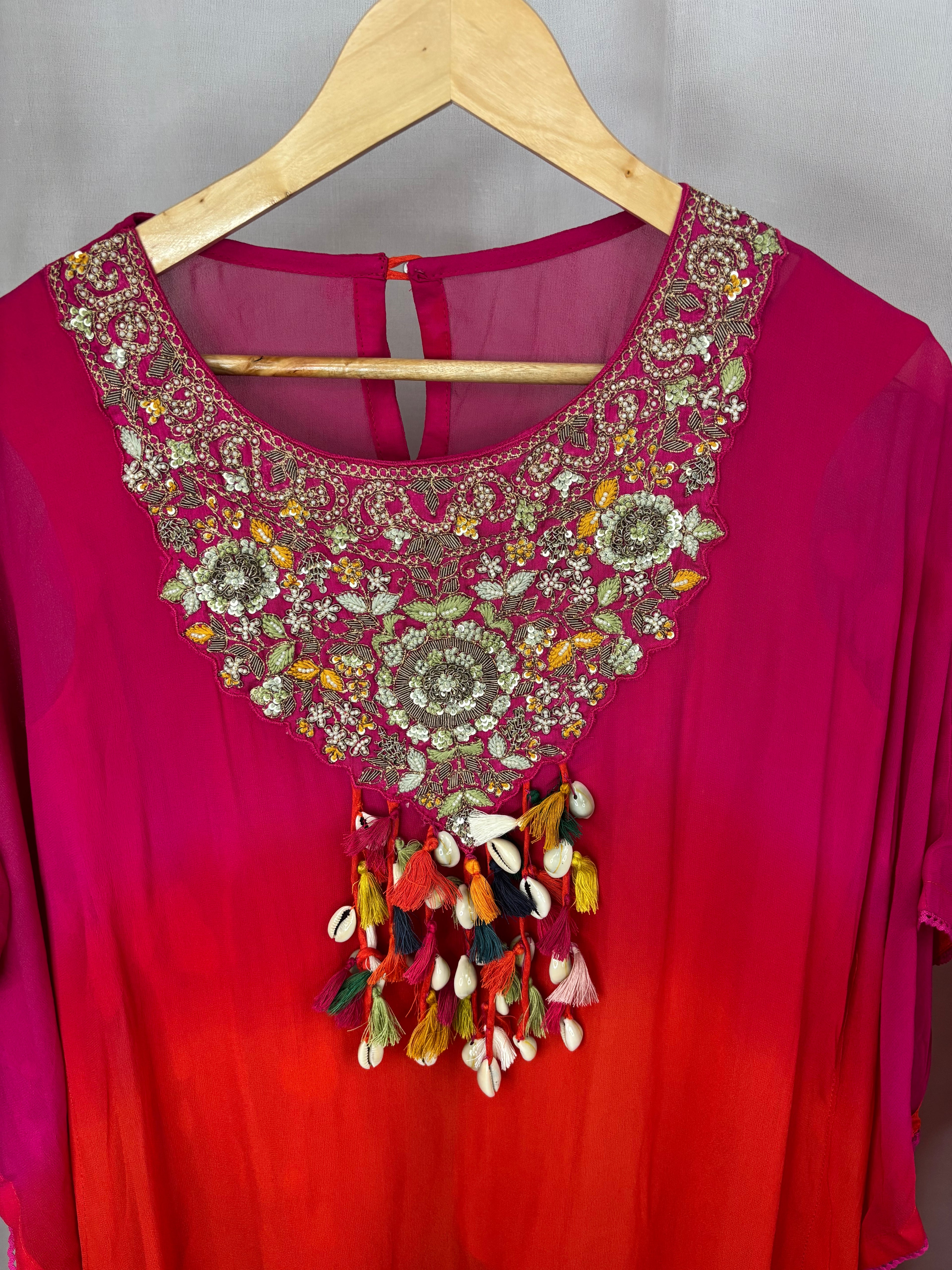 Red and pink blouse with intricate embroidery and tassels on a hanger.