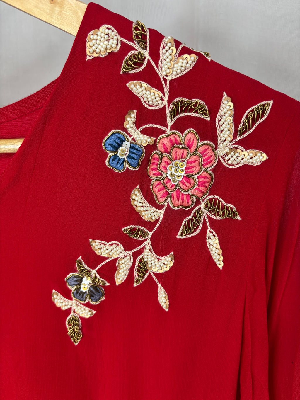 Red garment with floral embroidery on a wooden hanger against a gray background