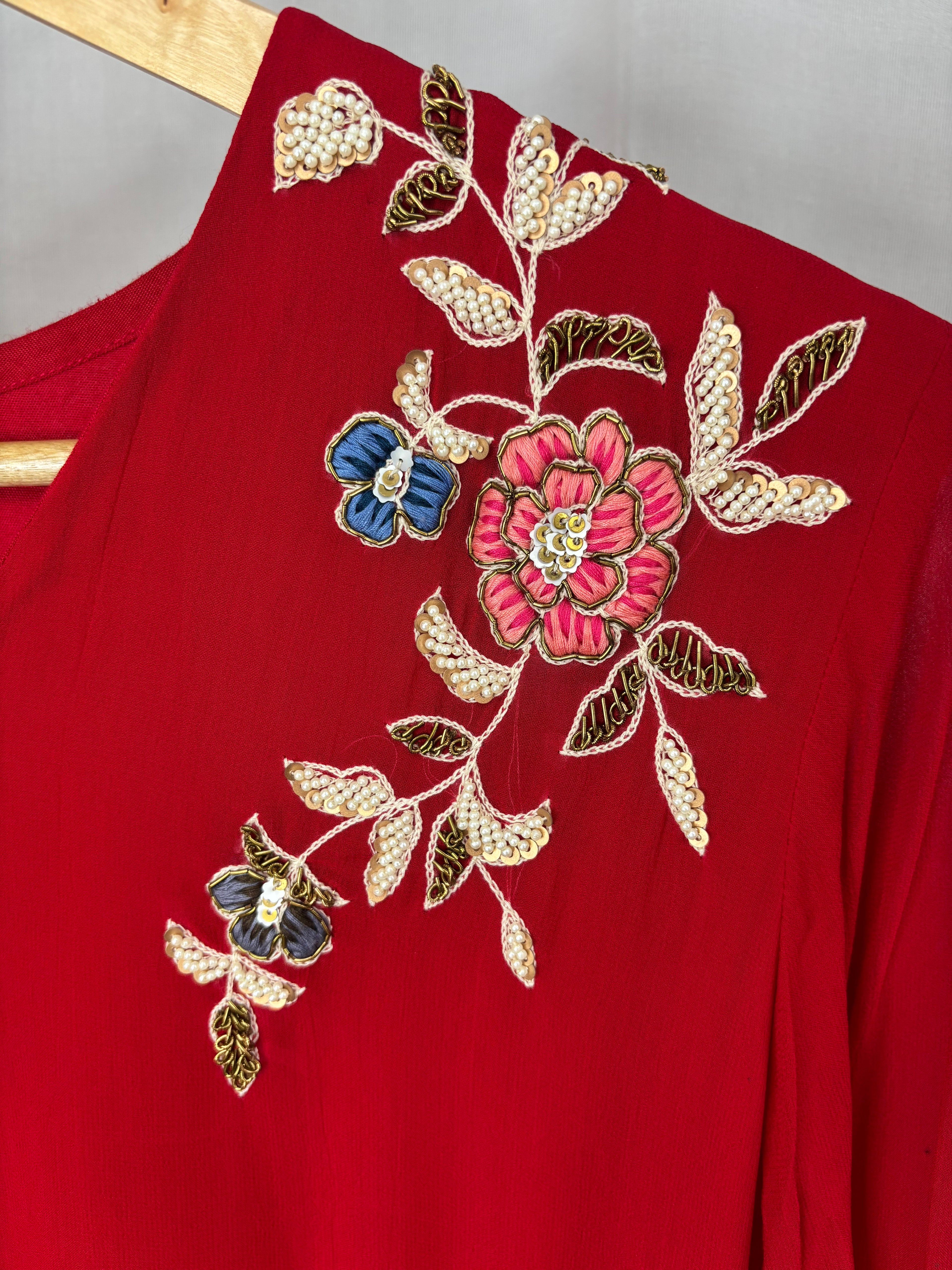 Red garment with floral embroidery on a wooden hanger against a gray background