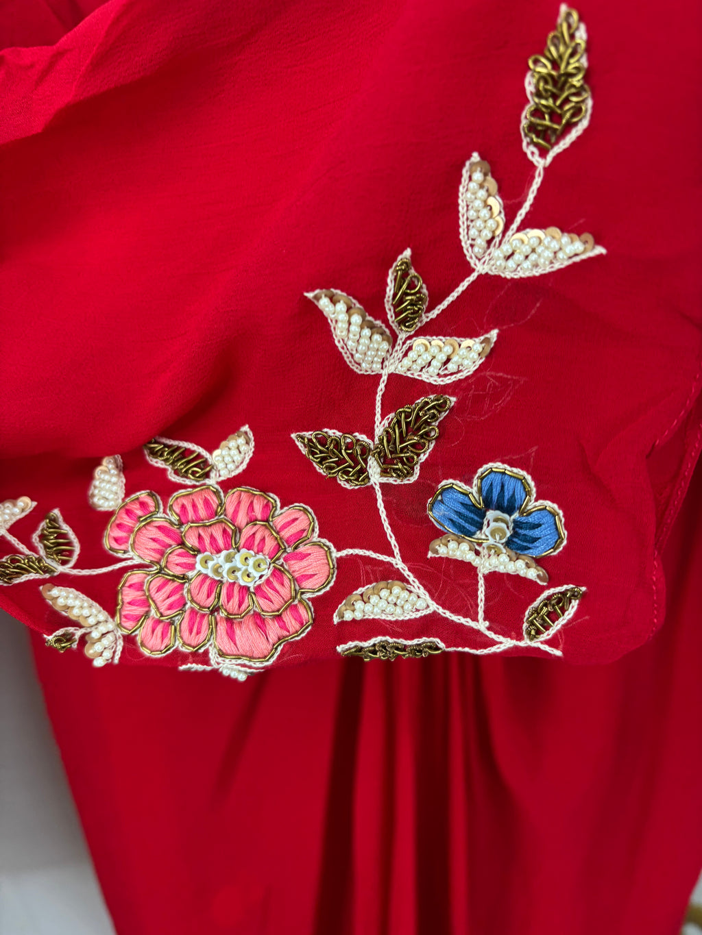 Red fabric with floral embroidery featuring pink, blue, and gold colors.