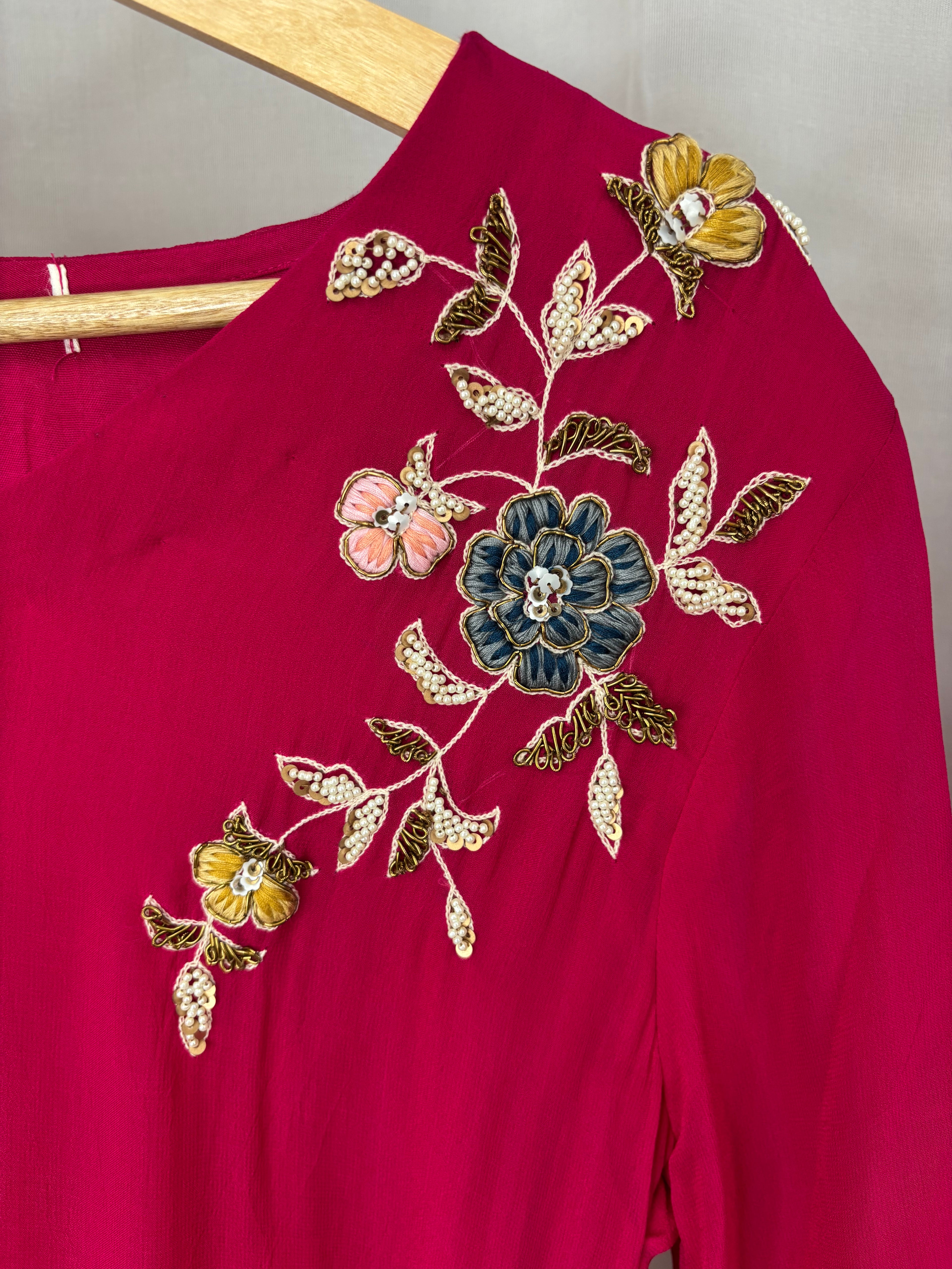 Red garment with floral embroidery on a wooden hanger against a neutral background