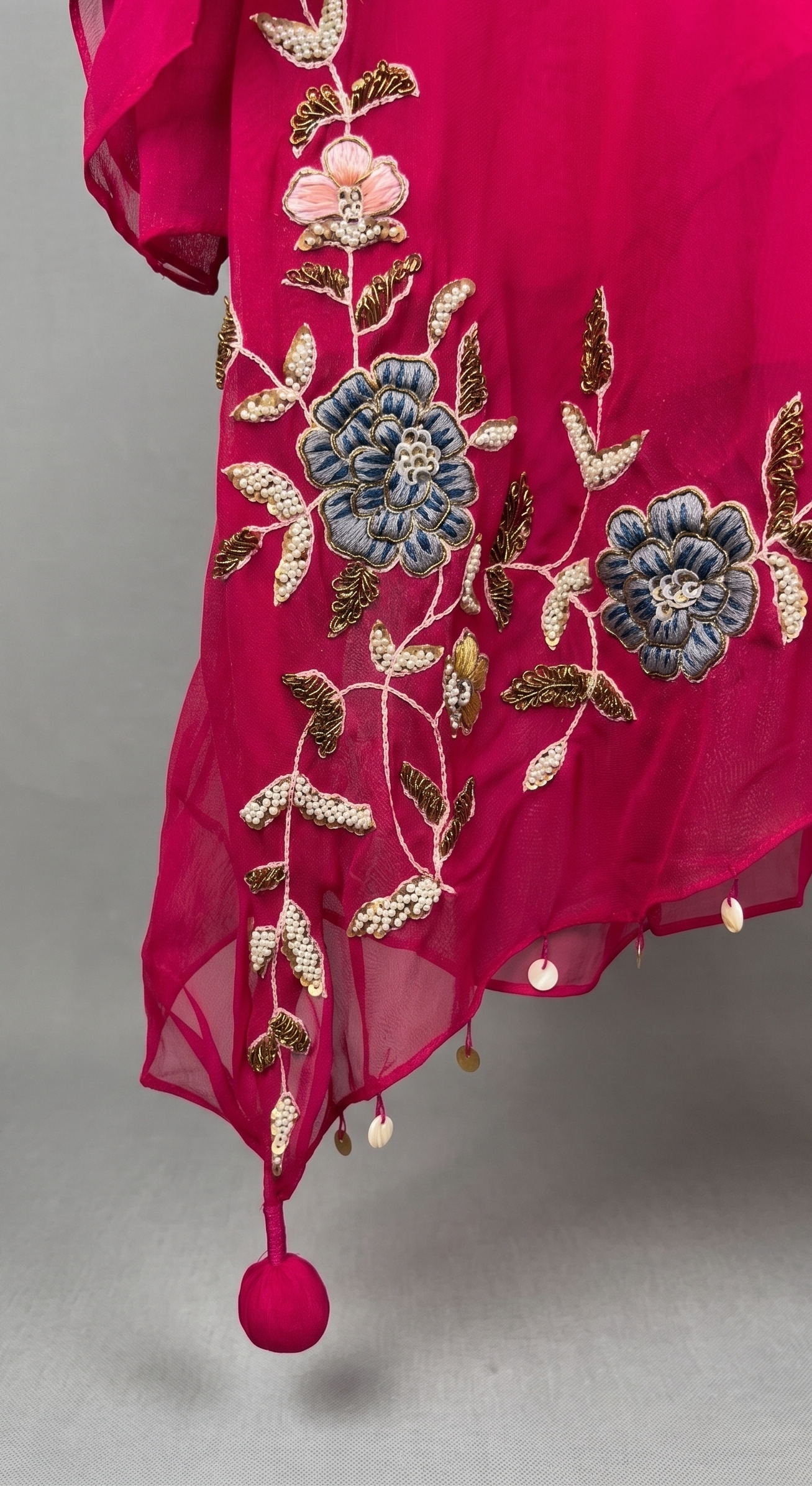 Pink fabric with floral embroidery and tassels on a gray background