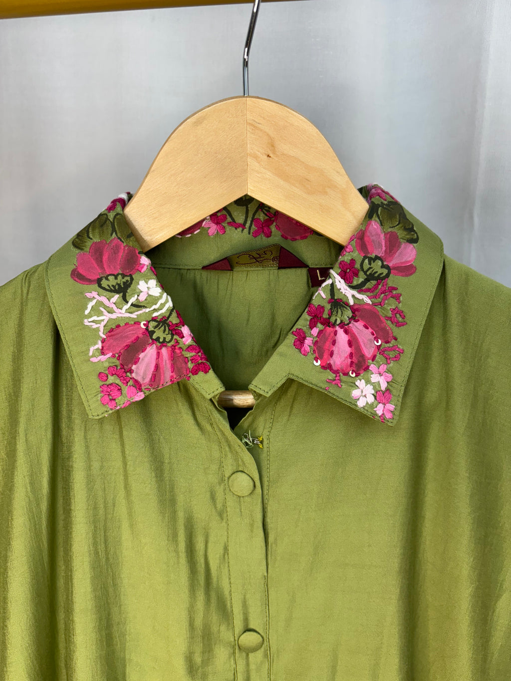 Green shirt with floral cuffs on a hanger against a white background