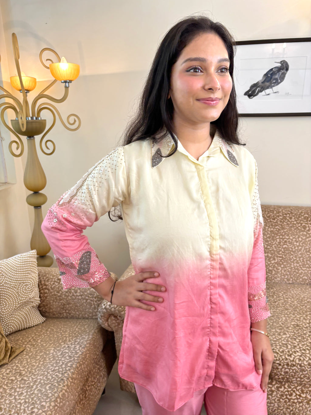 A woman wearing a cream and pink ombré button-up kurta with embroidered details on the collar and sleeves, standing in a living room setting.