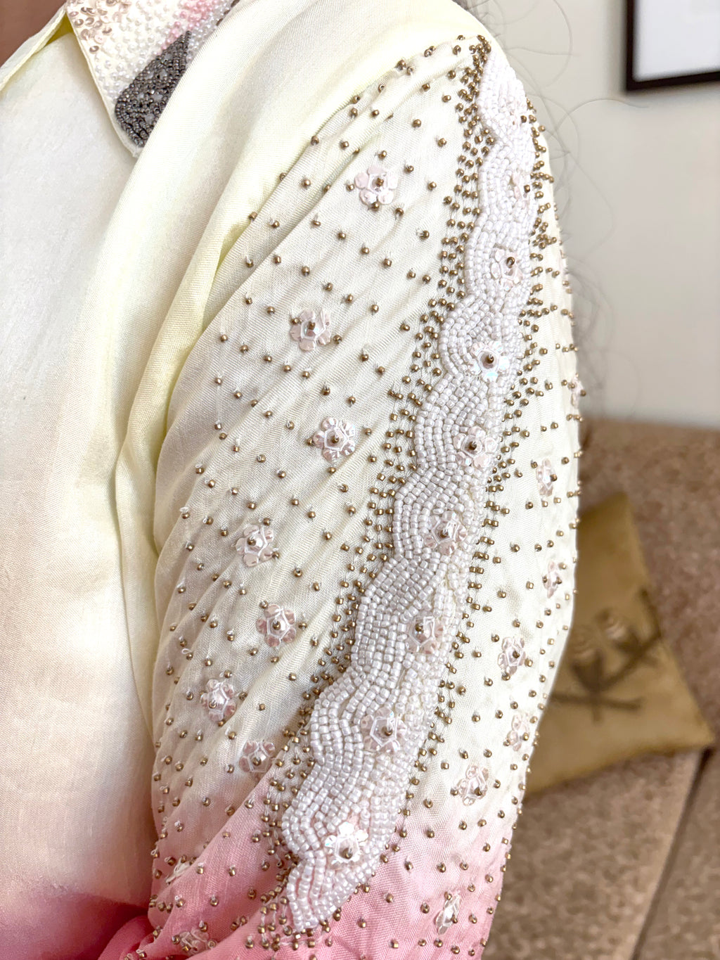 A close-up of a cream and pink draped fabric, likely a sari, heavily embellished with intricate silver beadwork, sequins, and floral embroidery.