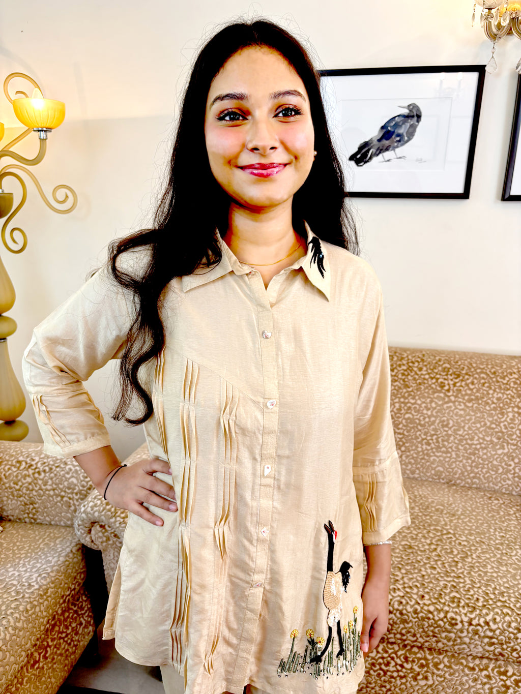 A woman wearing a light beige linen shirt with vertical stripes and a goose print near the hem, standing in a living room setting.