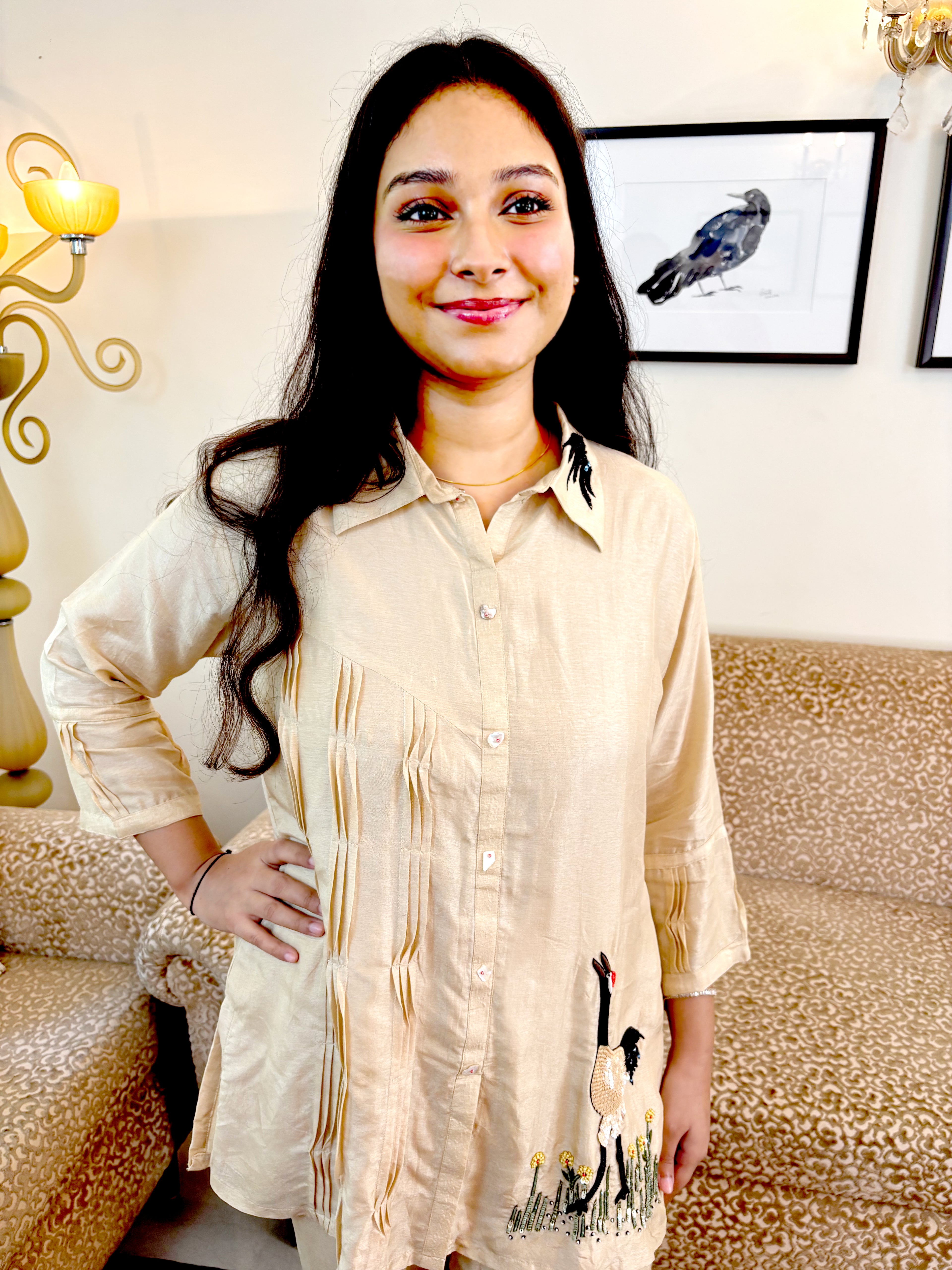A woman wearing a light beige linen shirt with vertical stripes and a goose print near the hem, standing in a living room setting.