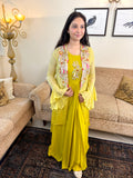 A woman wearing a bright yellow traditional dress with a matching embroidered light yellow cardigan, standing in a living room with patterned sofas and a rug.